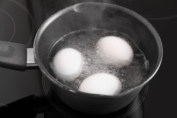 Cooking pot with boiling eggs on stove in kitchen, closeup