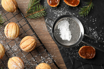 Delicious nut shaped cookies with powdered sugar and fir branches on wooden table, flat lay