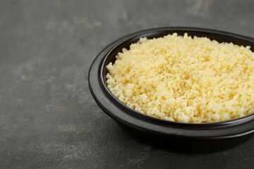 Bowl of tasty couscous on grey table, closeup. Space for text