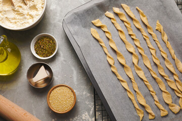 Baking sheet with homemade breadsticks and ingredients on grey marble table, flat lay. Cooking traditional grissini