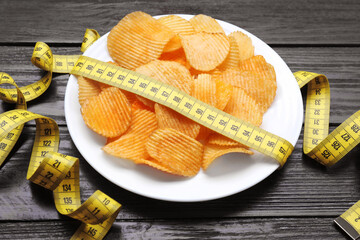 Plate with potato chips and measuring tape on wooden table. Weight loss concept