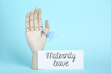 Wooden mannequin hand, pacifier and card with phrase Maternity Leave on light blue background....