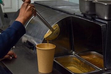 Restaurant kitchen employee pouring soup into a take out paper container