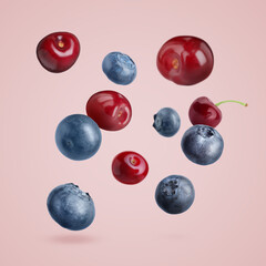 Blueberries and cherries falling on pale pink background