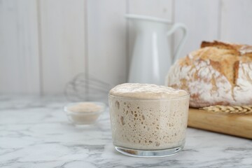 Glass jar with sourdough on white marble table. Space for text