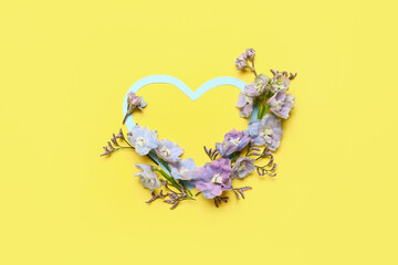 Blank heart-shaped frame and beautiful delphinium flowers on yellow background