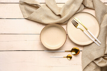 Plate, bowl and set of cutlery on white wooden background