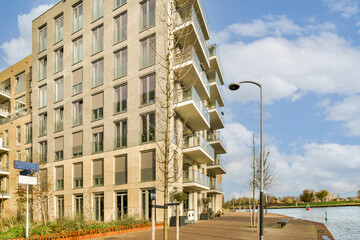 an apartment building next to a body of water with trees and bushes in the fore - part of the photo