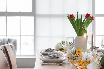 Beautiful table setting for International Women's Day celebration with different flowers in interior of light room