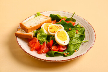 Plate of delicious salad with boiled eggs and salmon on beige background