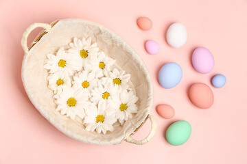 Fototapeta na wymiar Wicker basket with chrysanthemum flowers and painted Easter eggs on pink background