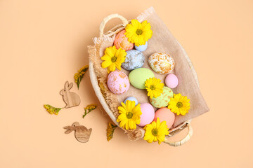 Wicker basket with painted Easter eggs, bunnies and chrysanthemum flowers on beige background