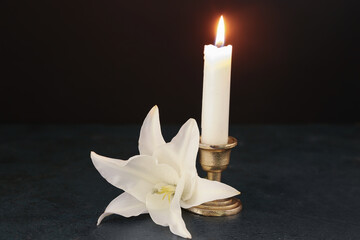 White lily flower and burning candle on dark table