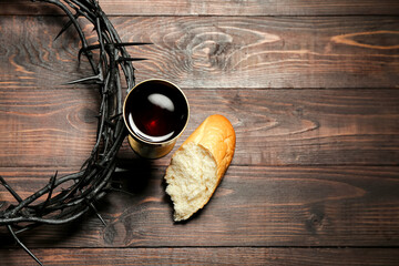Crown of thorns with cup of wine and bread on wooden background