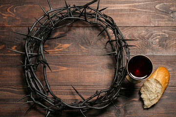 Crown of thorns with cup of wine and bread on wooden background