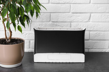 Air purifier and houseplant on table near white brick wall