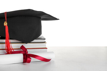 Graduation hat with diploma and books on table against white background