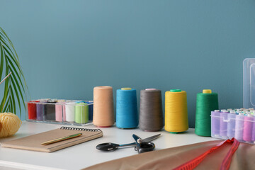 Notebook with scissors and thread spools on table in atelier, closeup