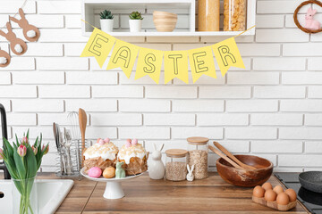 Cakes, Easter bunnies and tulip flowers on kitchen counter near white brick wall