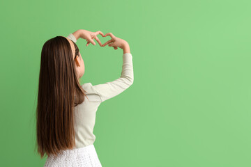 Cute little girl making heart with her hands on green background, back view