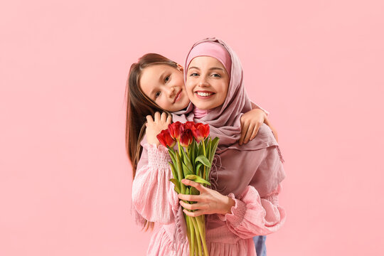 Little girl and her Muslim mother with tulips hugging on pink background