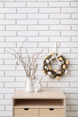 Table with willow branches in vase, toy rabbits and Easter wreath on white brick wall © Pixel-Shot