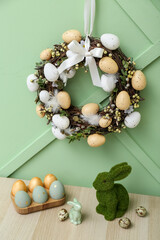 Table with Easter rabbits, eggs and wreath on green wall © Pixel-Shot