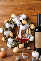 Bottle of wine, glass and Easter wreath on wooden background