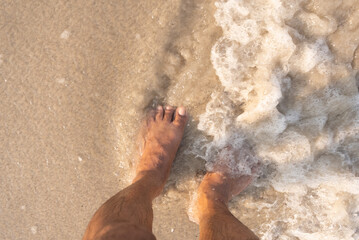Man's feet on the sand, beach, sea, waves, on summer vacation.
