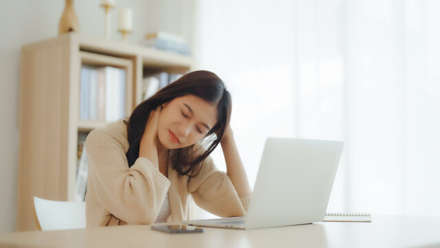 Office syndrome concept. Young asian woman feeling pain in neck and shoulder after working on computer laptop for a long time. She stretches to relax her muscles