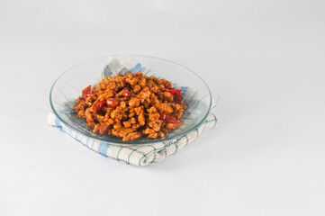 Fototapeta na wymiar sliced tempeh fried dry with chilies and peanuts or orek tempe served on a small plate with a napkin isolated on a white background