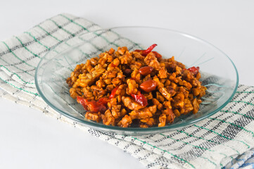 sliced tempeh fried dry with chilies and peanuts or orek tempe served on a small plate with a napkin isolated on a white background