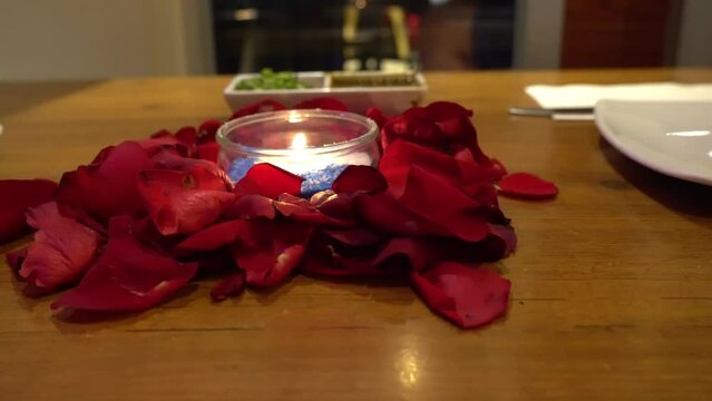 centerpiece arrangement made of red rose petals together with a candle light in a glass vase on a romantic evening for dinner