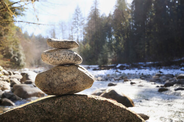Rock pile or stack in front of defocused river and forest on a sunny day. Pebble tower or rock pyramid. Concept for relaxing, zen, spiritual or yoga. Nature background. Selective focus on rocks. © Petra Richli