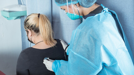 A doctor checks a patient's breathing with a stethoscope on her back. Checking up for signs of...