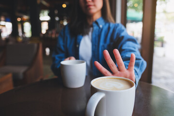 Closeup of a young woman making hand sign to refuse latte coffee