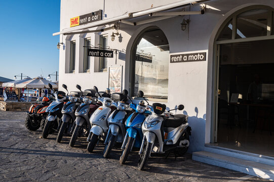 Photo of a row of scooters for rent at a RML car rental agency (rent a moto) at the ferry port of Pirikia. Scooters are a popular budget rental choice.