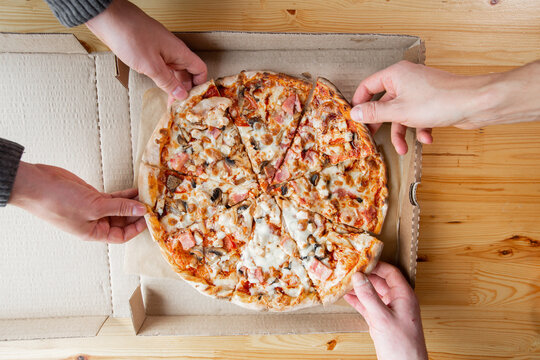 three people taking slices of pizza out of the box. fast delivery of food. packaging for fast food. top view