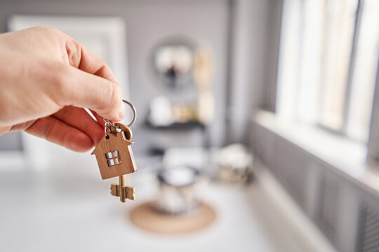 Key with house shaped keychain. Modern light lobby interior. Mortgage concept. Real estate, moving home or renting property.