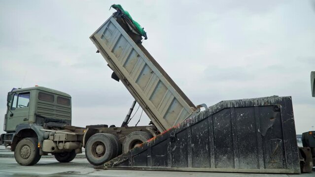 Dump truck unload cargo into special container, side view
