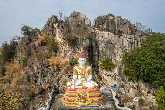 The white Buddha statue with rock mountain in the background at Tham Champathong monastery, Ratchaburi, Thailand