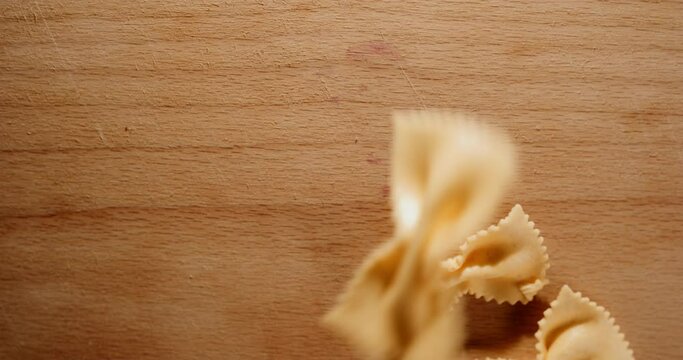 throwing uncooked butterfly pasta onto a wooden table close up in studio lighting