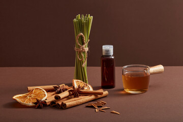 Brown bottle without label, lemongrass, cinnamon sticks, dried orange slice and anise on dark...