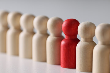 Red figure in row of many common wooden people figures.