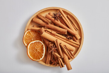 Top view of cinnamon sticks, anise and dried orange slices put on wooden dish, isolated on white background. Medicinal herbs, cooking spices, cosmetic flavorings