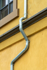 Bending gray metal rain gutter on side of orange stucco cement building with visible window in...