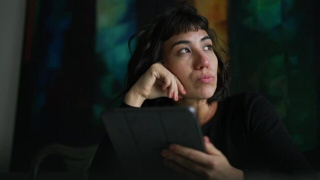 Pensive hispanic woman holding tablet device. Thoughtful South American girl using digital modern technology having a breakthrough idea