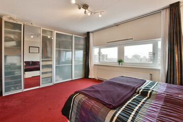 a bedroom with red carpeting and white doors leading to the bed area, there is a large window that...