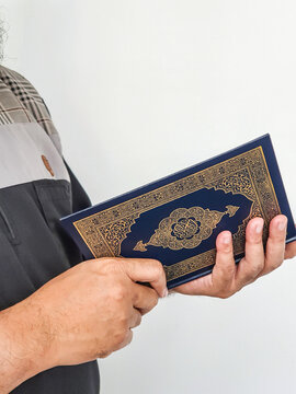 Ramadan Kareem, Eid Mubarak or Islamic concept. The Islamic holy book, Quran or Kuran, on grey background. Arabic words on the book means "Holy Quran". Hand holding.