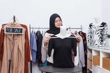 Young Asian muslim woman selling clothes online on social media, she is measuring the size of a black shirt